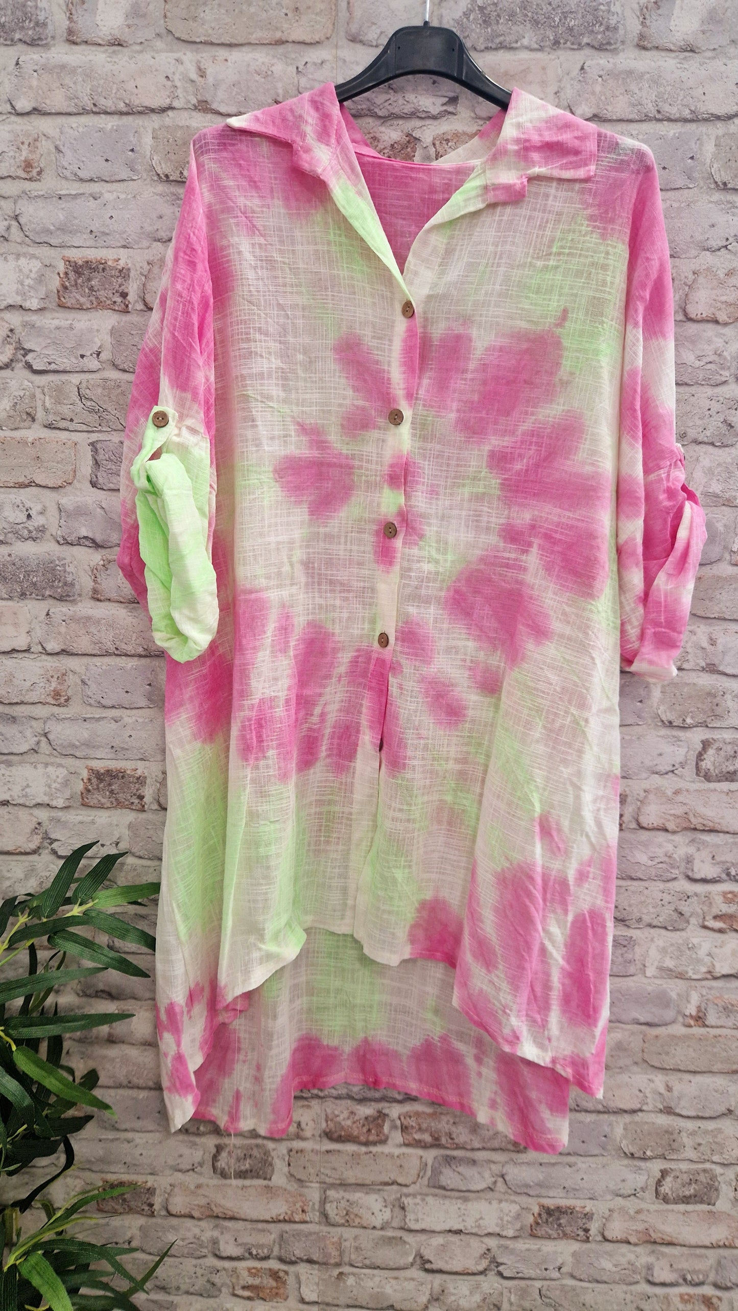 Tie Dye Cotton Shirt with pink and green patterns on a hanger in front of a brick wall.