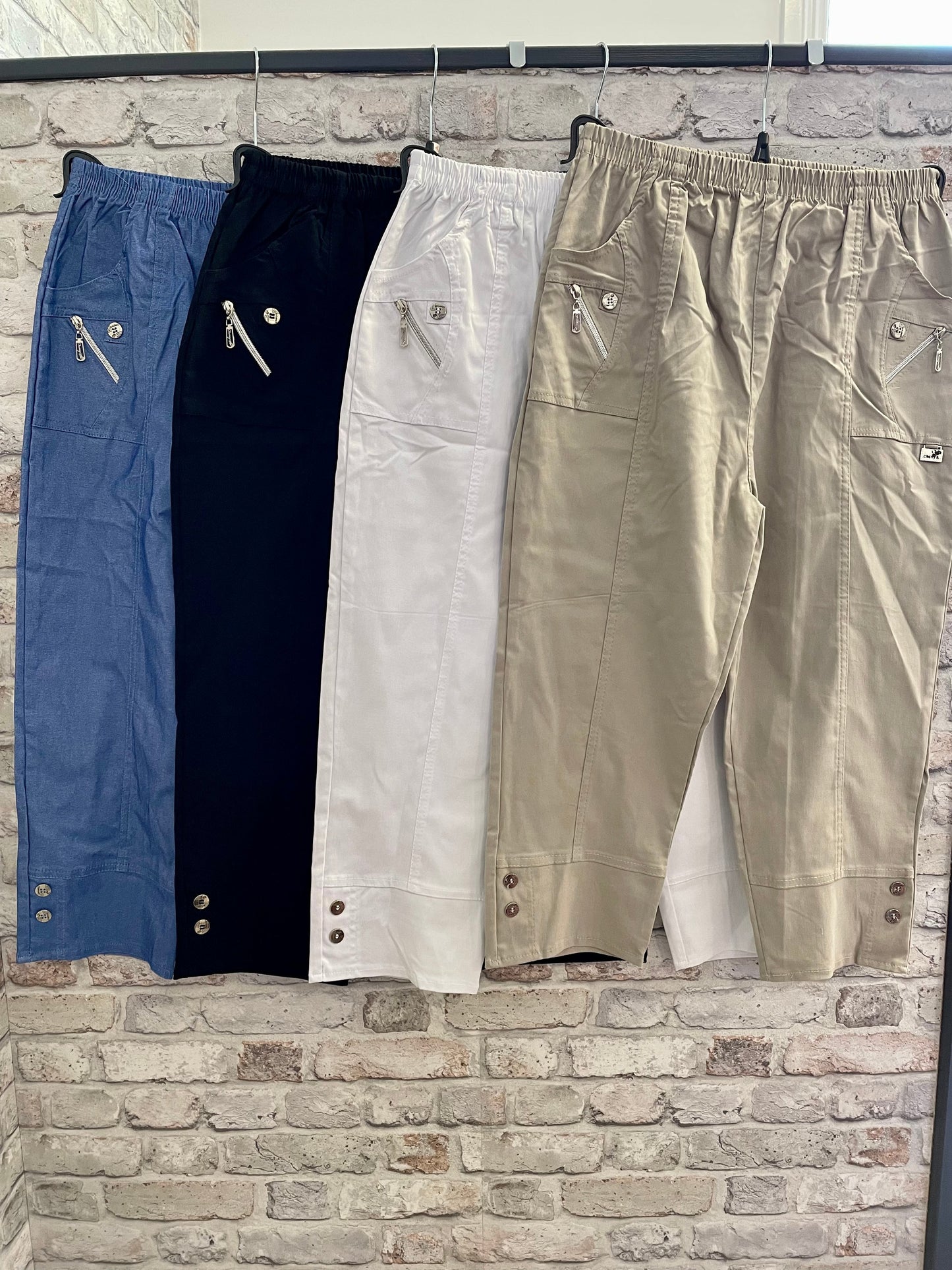 Cropped stretch trousers with zip and button details in blue, black, white, and beige.