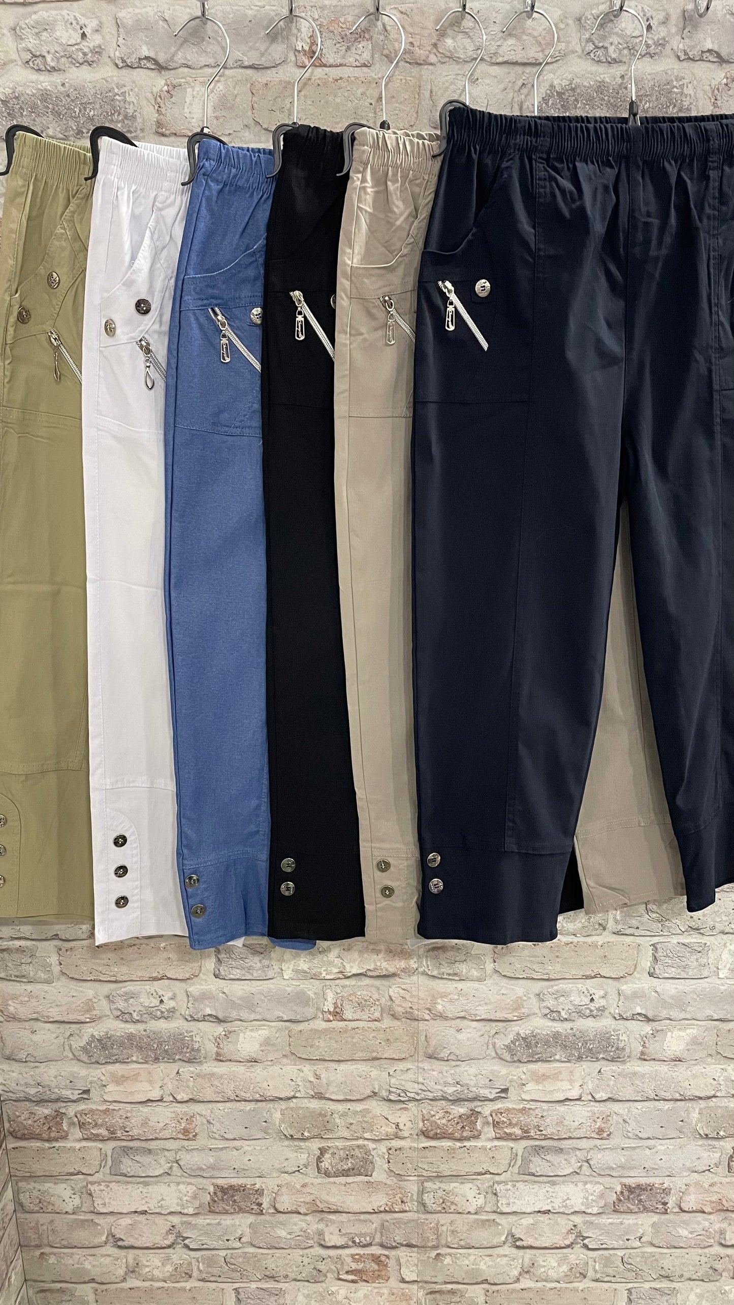 Cropped stretch trouser with button and zip details in various colors.