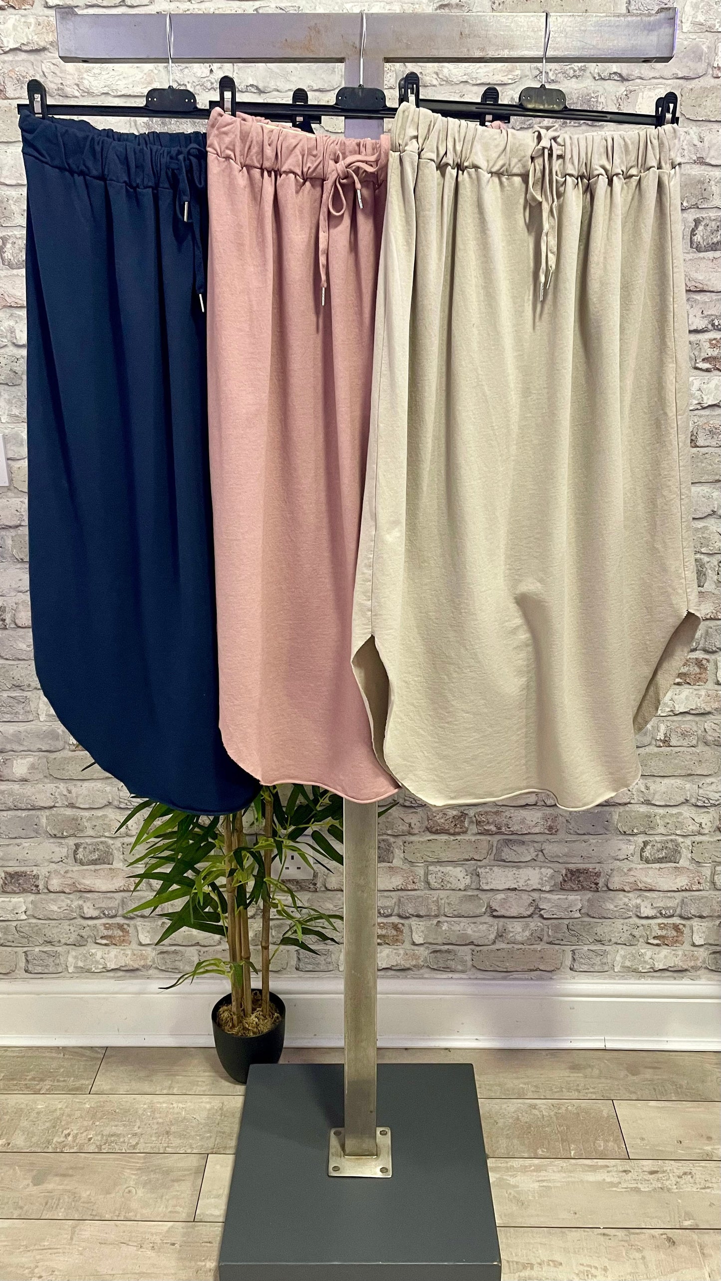Three curve hem skirts in navy, pink, and beige on a stand, made of cotton and elastane.