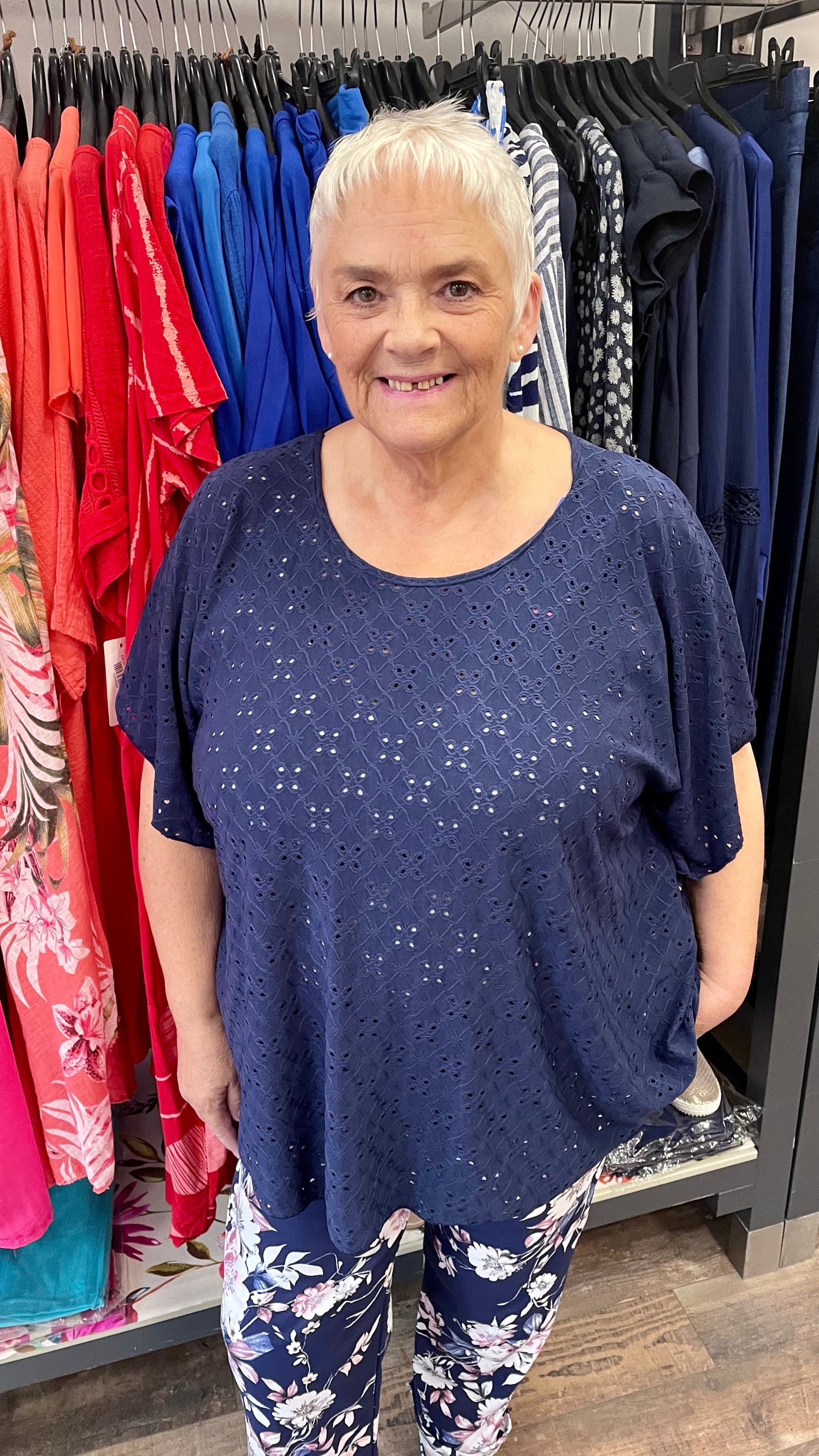 Round Neck Broderie Top in navy with short sleeves displayed on a smiling person in a clothing store.