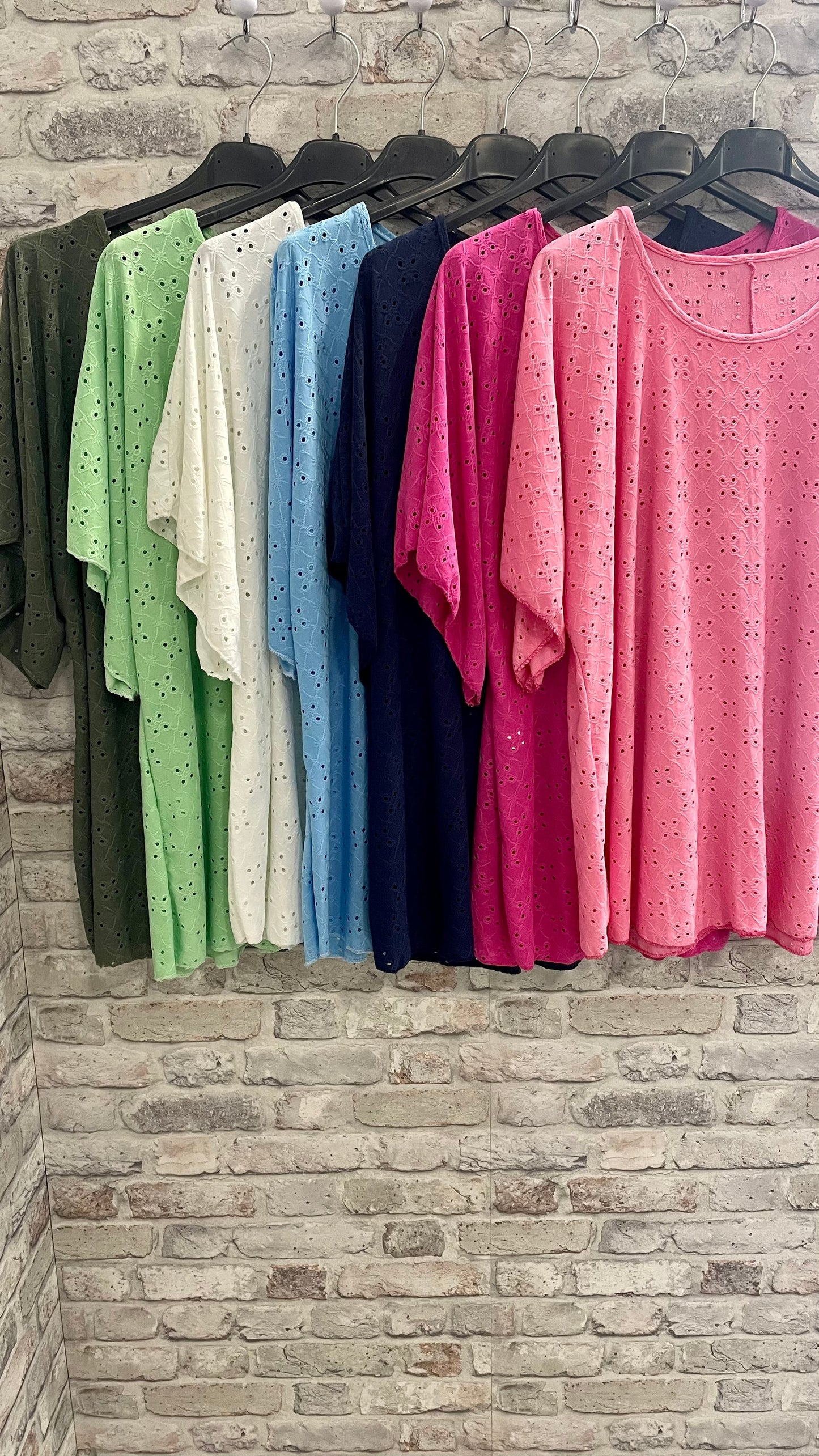 Round Neck Broderie Tops in assorted colors hanging on a rack.