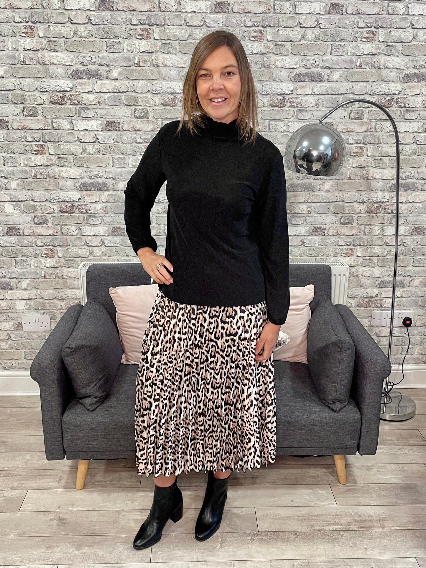 Woman wearing a black metallic frill neck top with a patterned skirt, standing in a stylish living room.