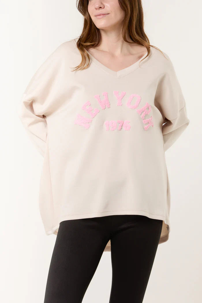 V-neck sweater with "New York" text in pink, chic and comfortable design.
