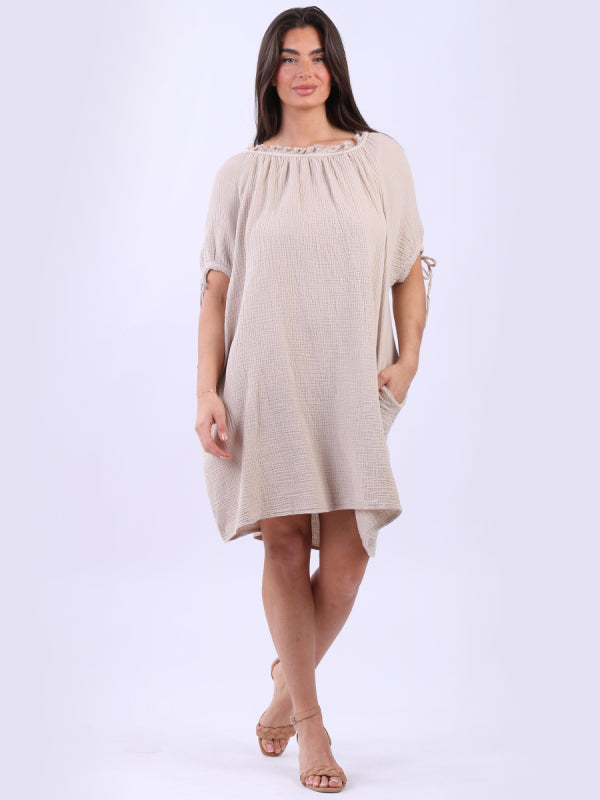 Cheesecloth drawstring dress with ruched neck, tie knot, knotted balloon sleeves, and side pockets, made in Italy.