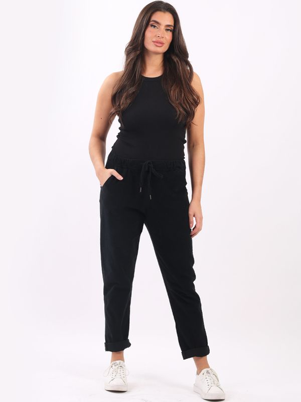 Woman wearing black cotton corduroy trousers with elastic waist and drawstring belt.