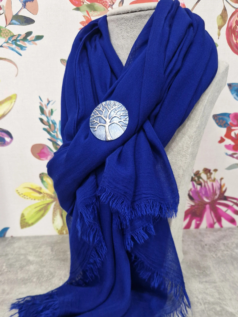 Royal blue scarf with decorative brooch on mannequin in floral backdrop.