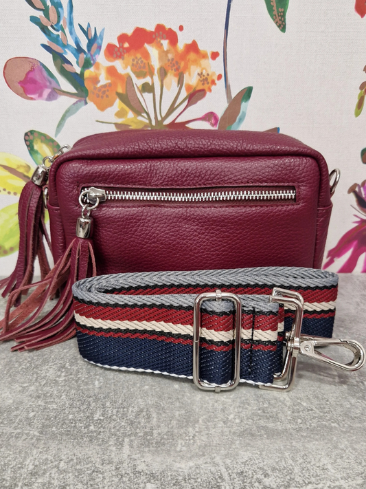 Burgundy leather bag with decorative strap on floral background.