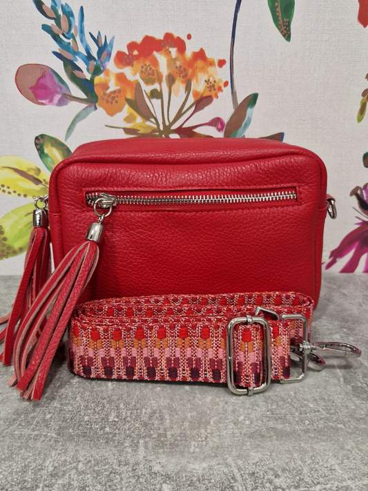 Red leather bag with decorative strap against floral background.