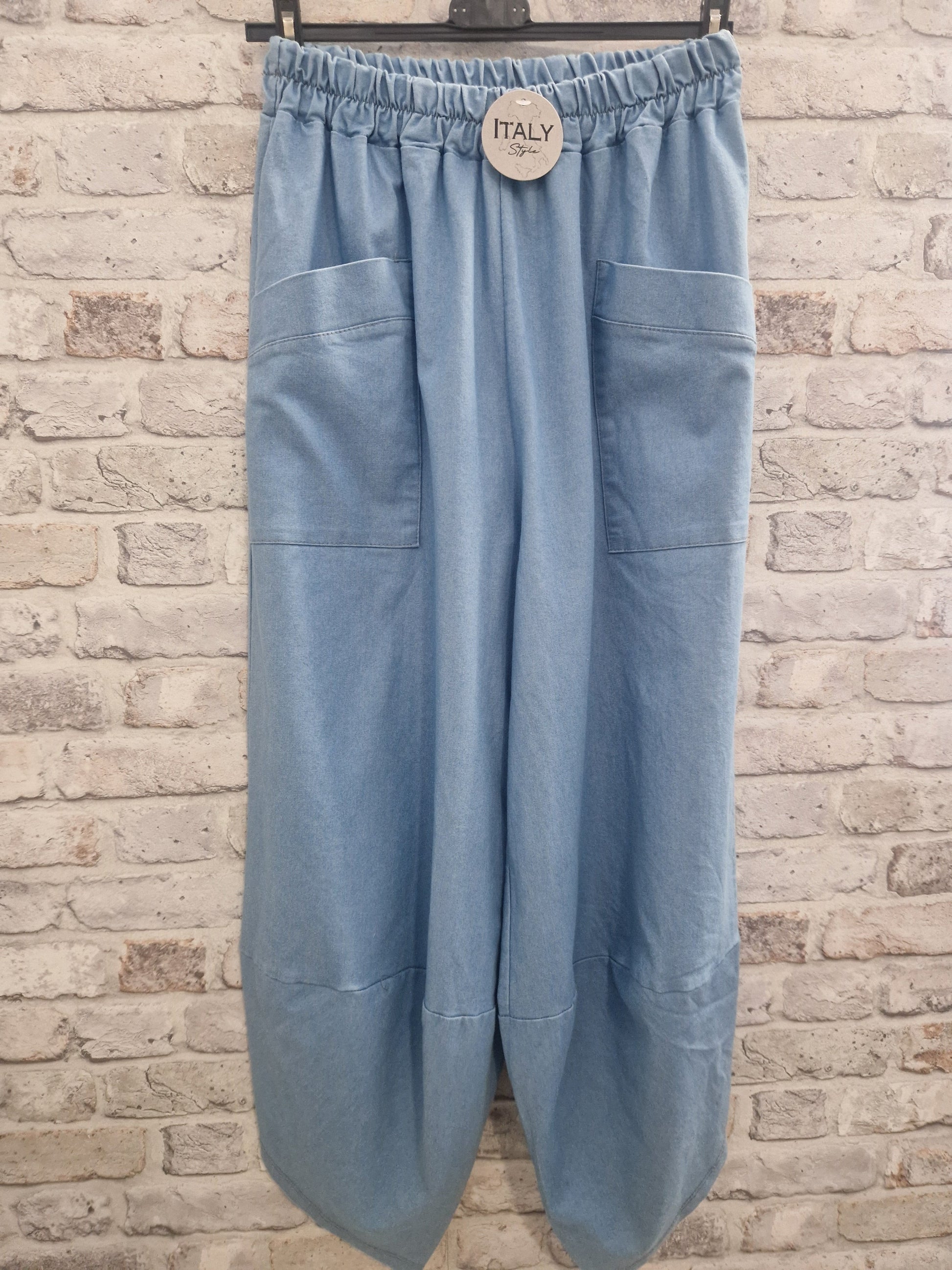 Denim harem trousers with relaxed fit and large front pockets against brick background.