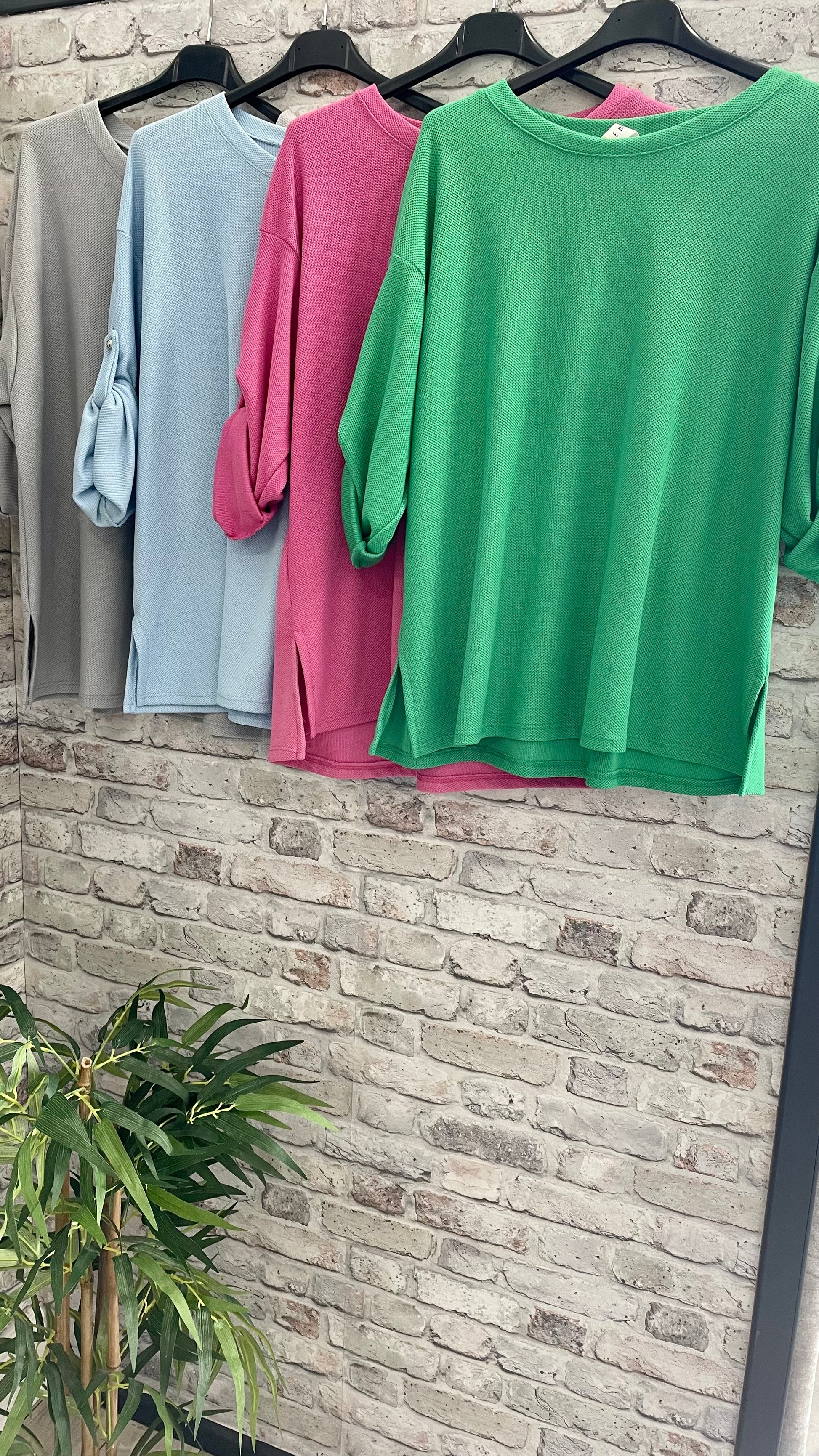 Waffle style side slit tops in gray, blue, pink, and green hanging on hangers.