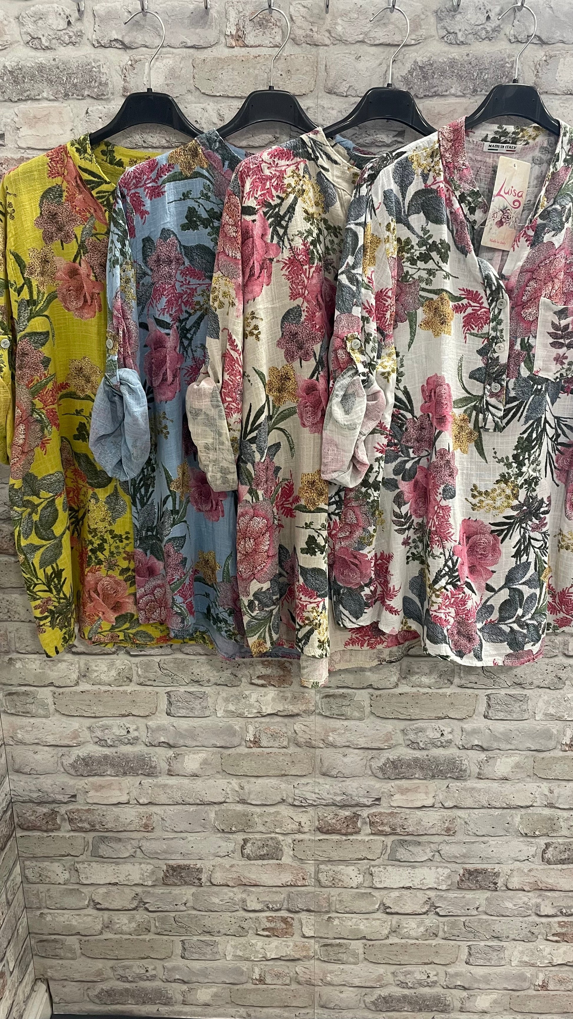 English Garden Grandad Shirt in floral patterns, 100% cotton, with single pocket, on hangers against brick wall.