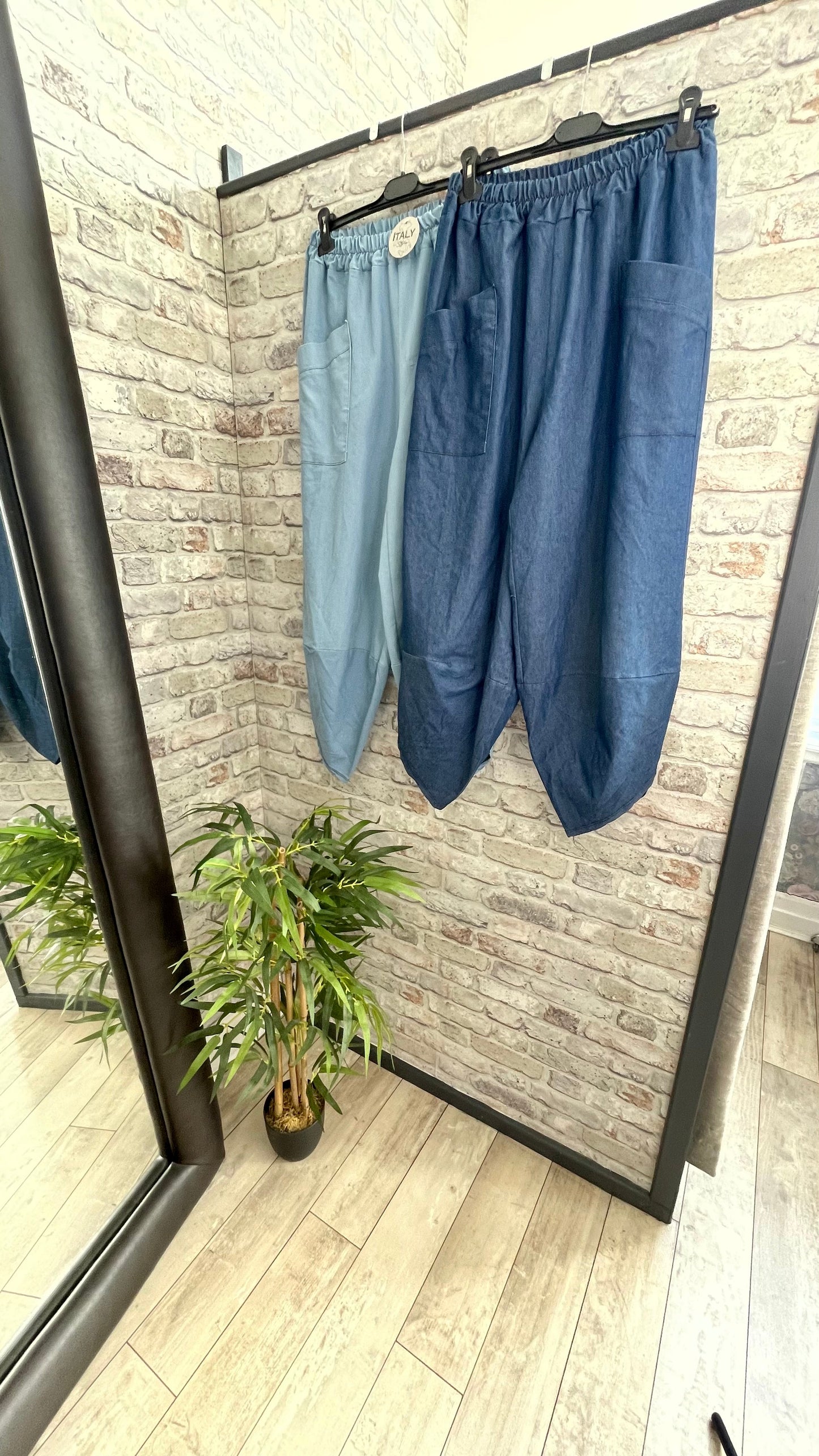 Denim harem trousers hanging in a stylish room with brick walls and a mirror.