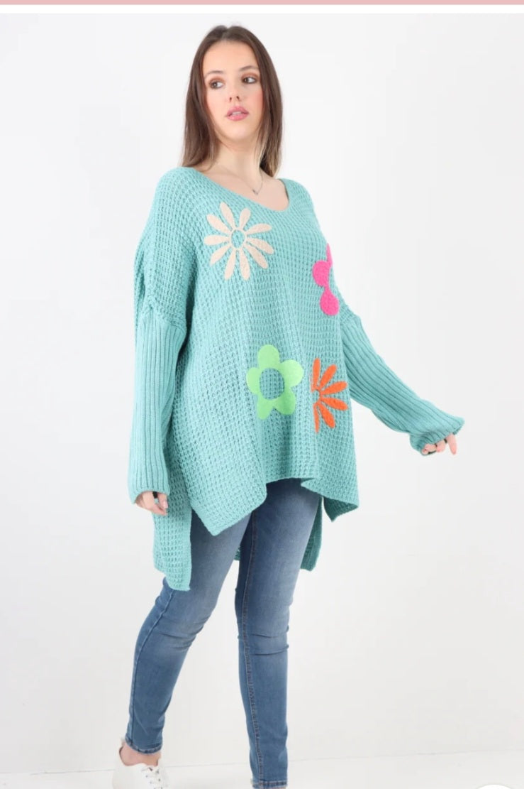 Side slit floral jumper in turquoise with colorful flower patterns and asymmetric hem.