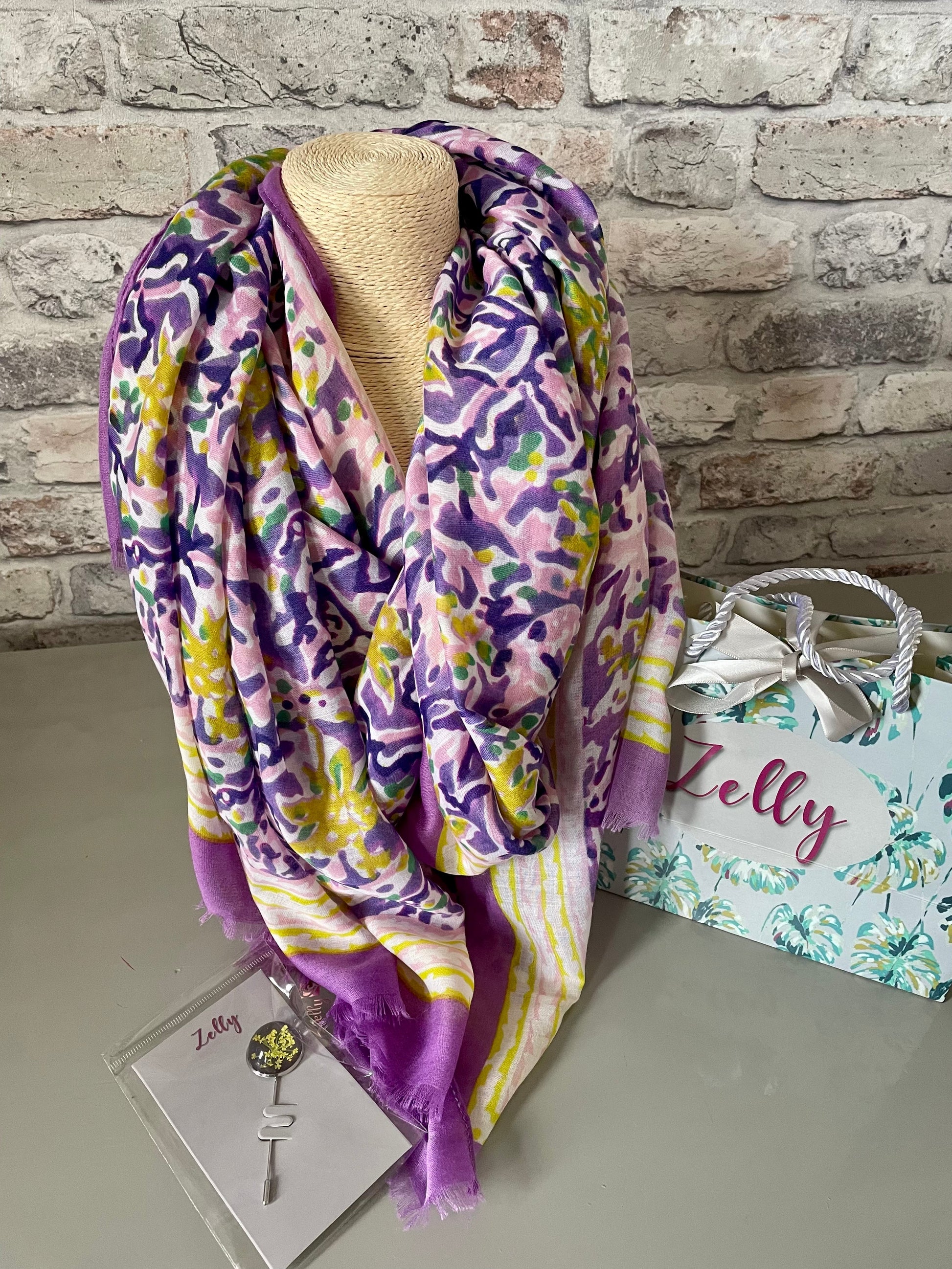Zelly Scarf with colorful design displayed on mannequin, gift bag in background.